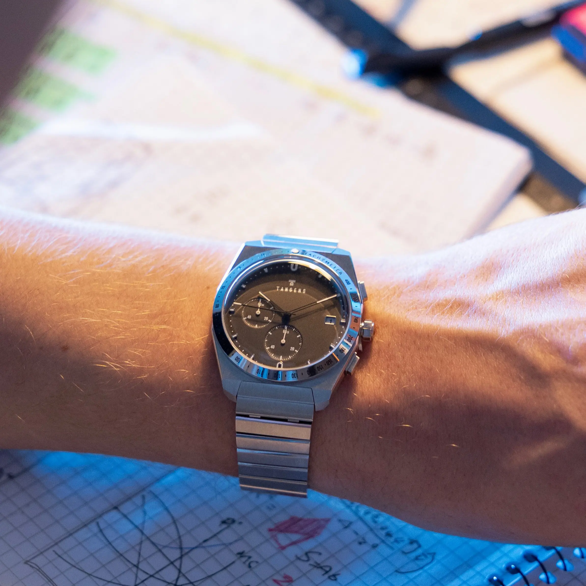 A Komposition Chronograph Black on a wrist over a notebook of sketches