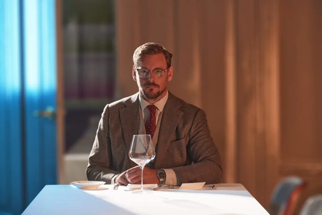 A man in a tweed jacket sits alone at a long dinner table