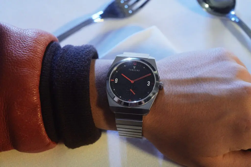 A Komposition Black on a wrist in a leather jacket sleeve, over a white tablecloth