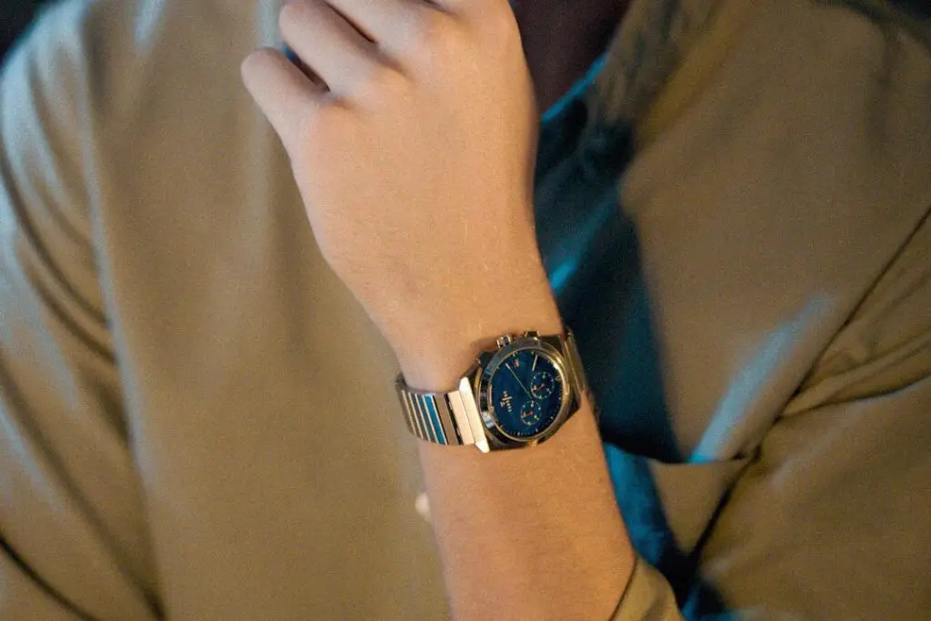 A man rests his chin on his hand, a Komposition Chronograph Cool Navy on his wrist